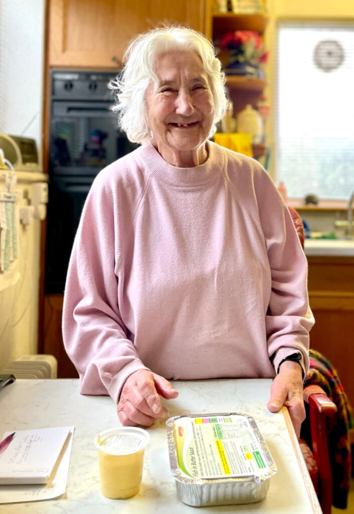 A photograph of a lady in her kitchen with a prepared ready meal