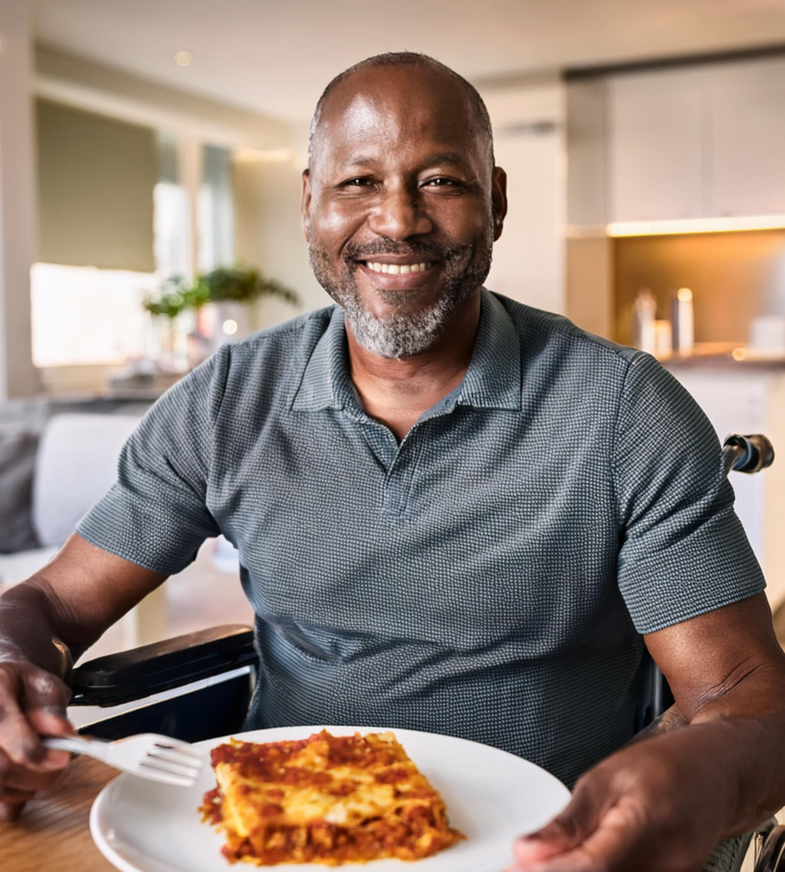 A photograph of a man in a wheelchair about to eat lasagne