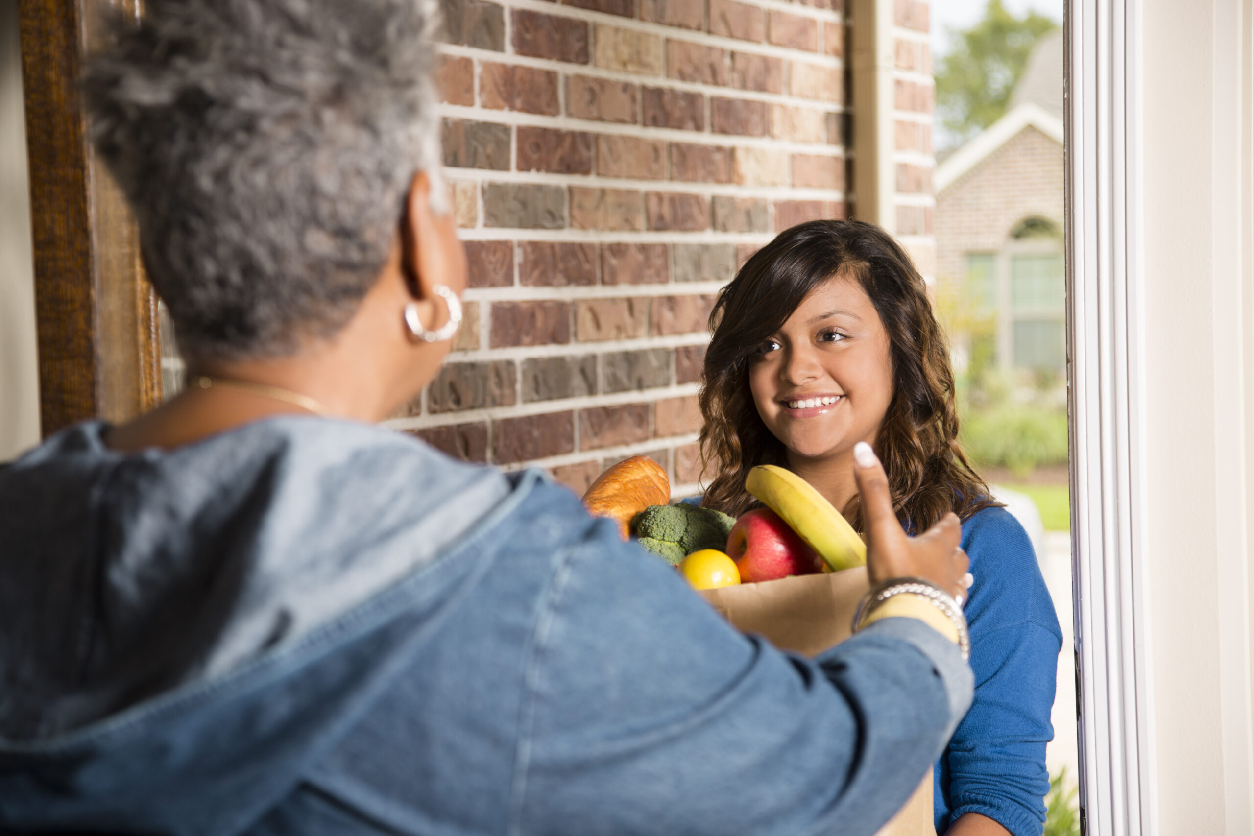 A young woman delivering a bag of groceries to a senior adult woman